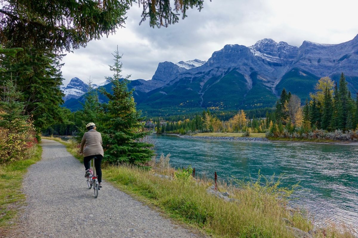 Man cycling past a river with snow capped mountains